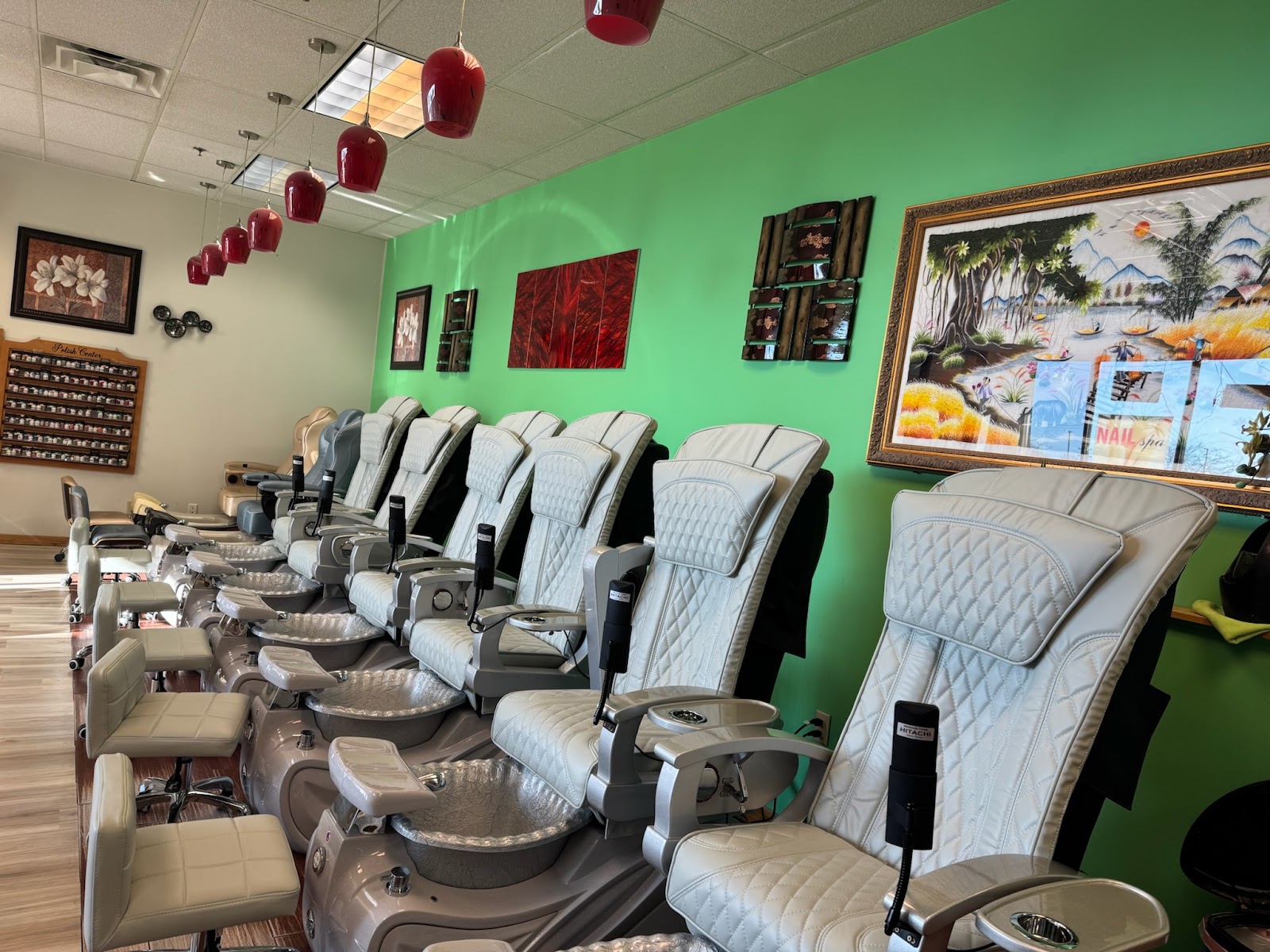 A row of white pedicure chairs along a bright green wall inside the salon